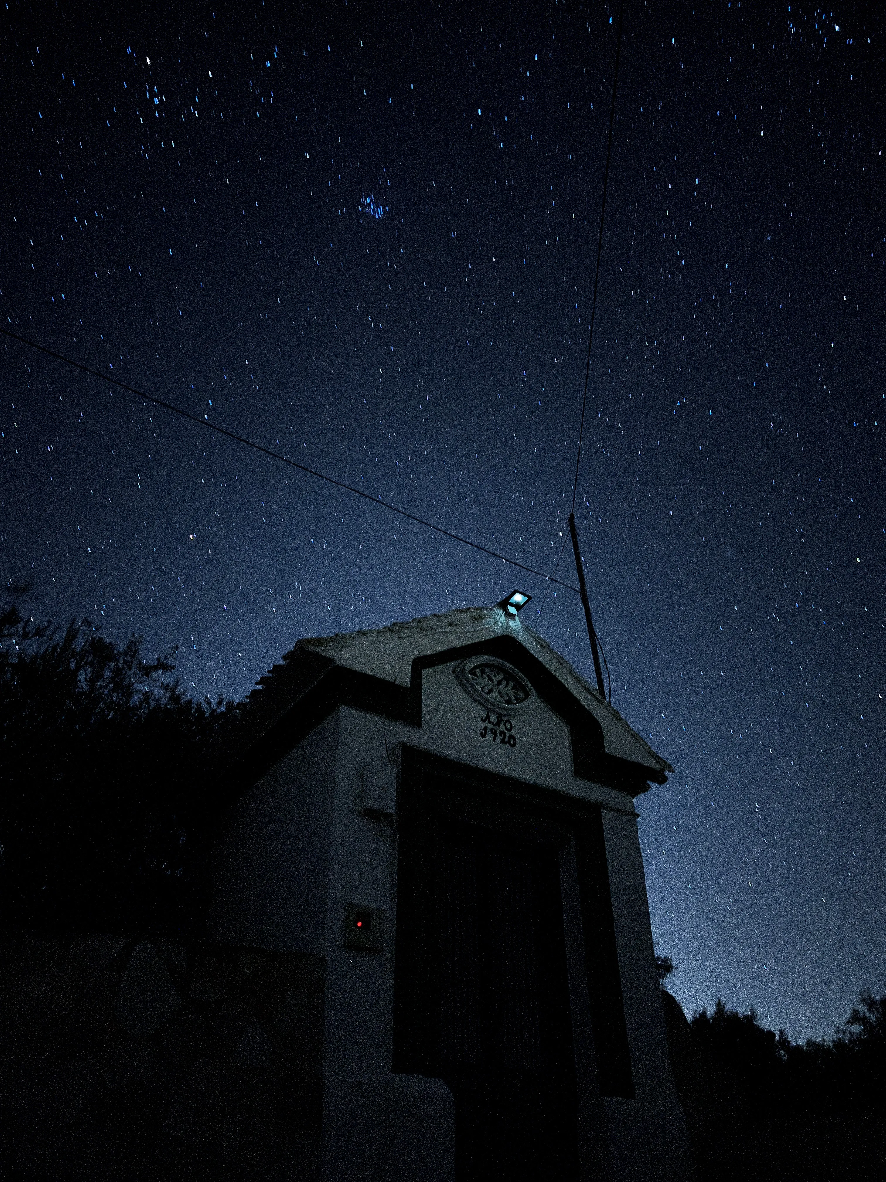 Pequeña edificación rural con foco LED deslumbrante bajo un cielo estrellado, claro ejemplo de contaminación lumínica