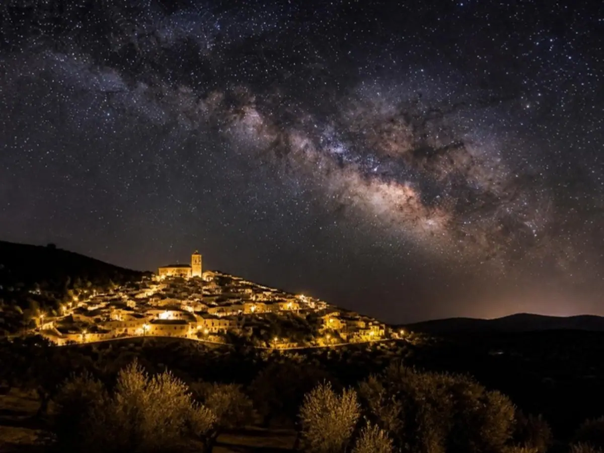 Pueblo blanco andaluz de noche con alumbrado apantallado bajo un cielo estrellado sin contaminación lumínica